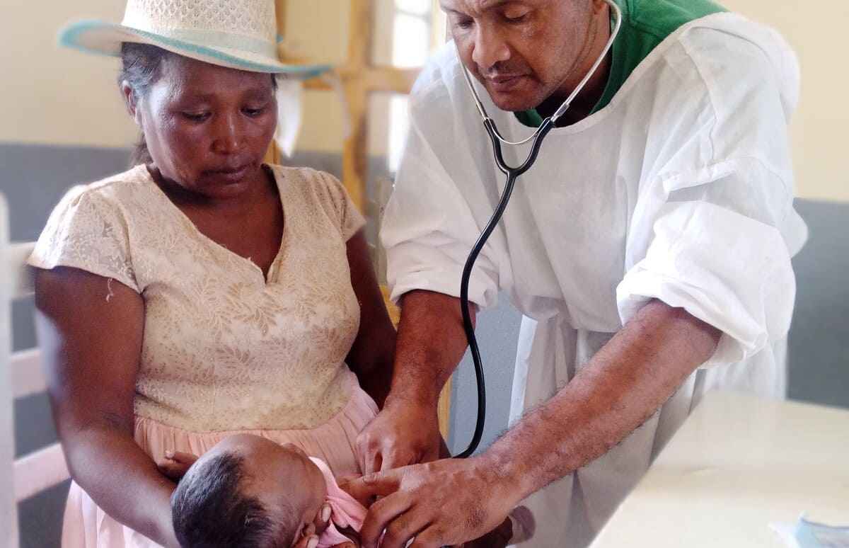 Un médecin examinant avec un stéthoscope un bébé tenu par sa mère