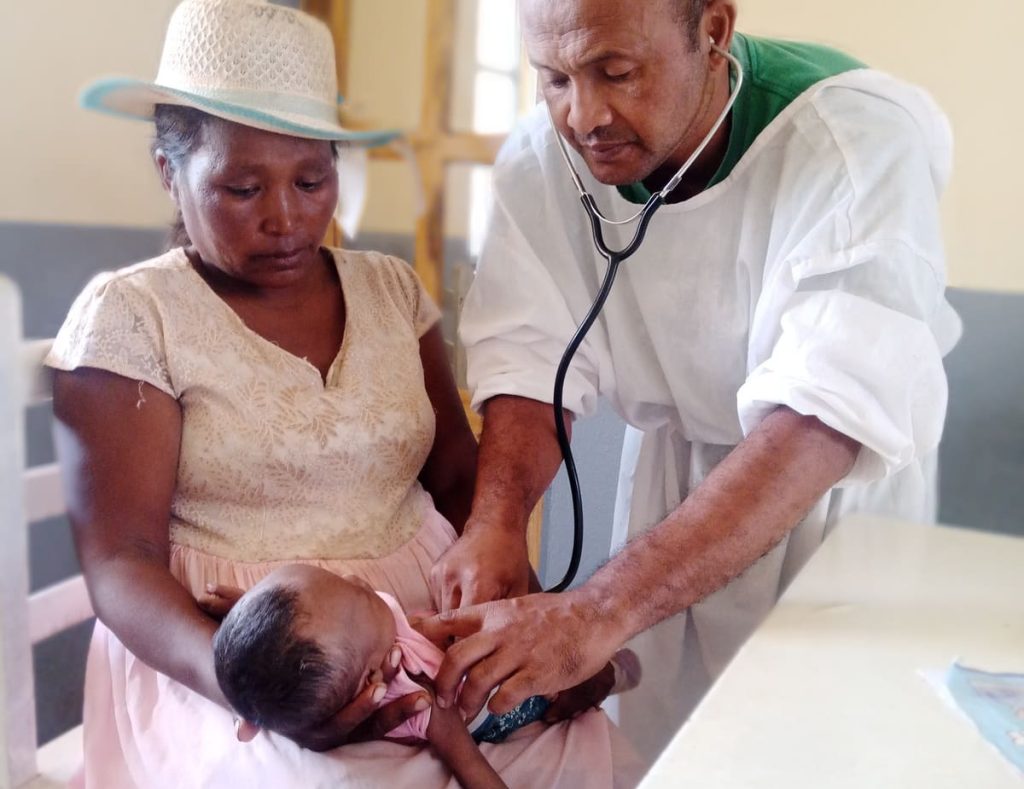 Un médecin examinant avec un stéthoscope un bébé tenu par sa mère