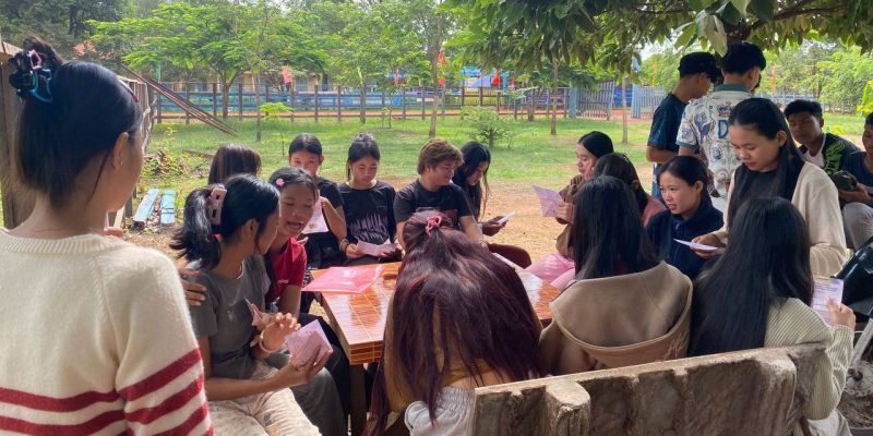 A Group Of Young People Reading Psea Leaflet Produced By The Regenerate Cambodia
